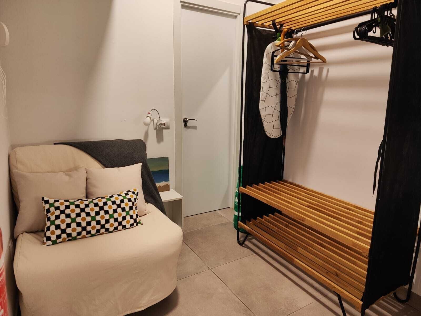 Une petite pièce agréable, dotée d’un lit, d’un banc en bois et d’un portant à vêtements.