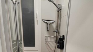 Ducha a ras de suelo con mampara de vidrio, alcachofa, ducha de mano y dispensador de jabón.
