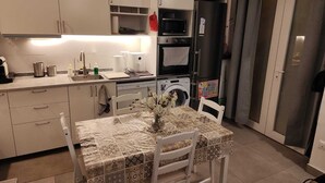 Una cocina compacta con armarios blancos, un microondas, un refrigerador y una lavadora.
