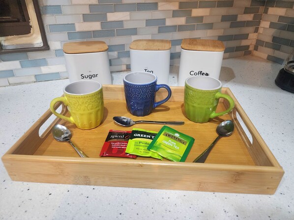 Una bandeja con tres tazas etiquetadas como 'Azúcar', 'Té' y 'Café', y dos bolsitas de té verde Twinings.