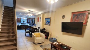 Una sala de estar con un sofá, una mesa de centro y un televisor. Se ve una escalera que lleva a otra habitación.