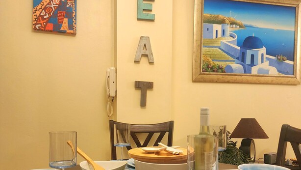 Una mesa de comedor dispuesta con platos, fuentes y cubiertos, un cuadro y letras decorativas que deletrean “EAT” en la pared.