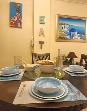 Una mesa de comedor dispuesta con platos, fuentes y cubiertos, un cuadro y letras decorativas que deletrean “EAT” en la pared.