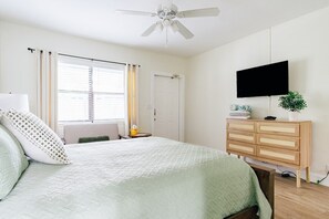 A bedroom with a bed, a dresser, a television, a ceiling fan, and a window with curtains.