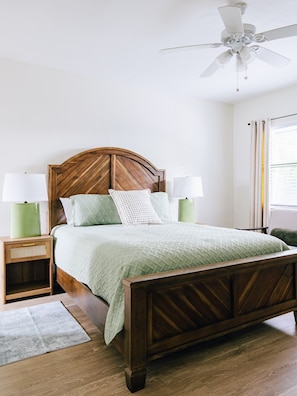 A bedroom with a wooden bed, two bedside tables with lamps, a ceiling fan, and a window with curtains.