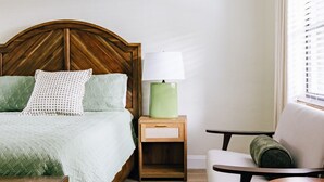 Quarto com cama de madeira, mesa de cabeceira com abajur, uma cadeira e janela com persianas.