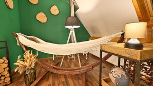 Eine Hängematze, die zwischen Holzbalken gespannt ist, eine Lampe auf einem Tisch und ein Globus auf einem Stativ.