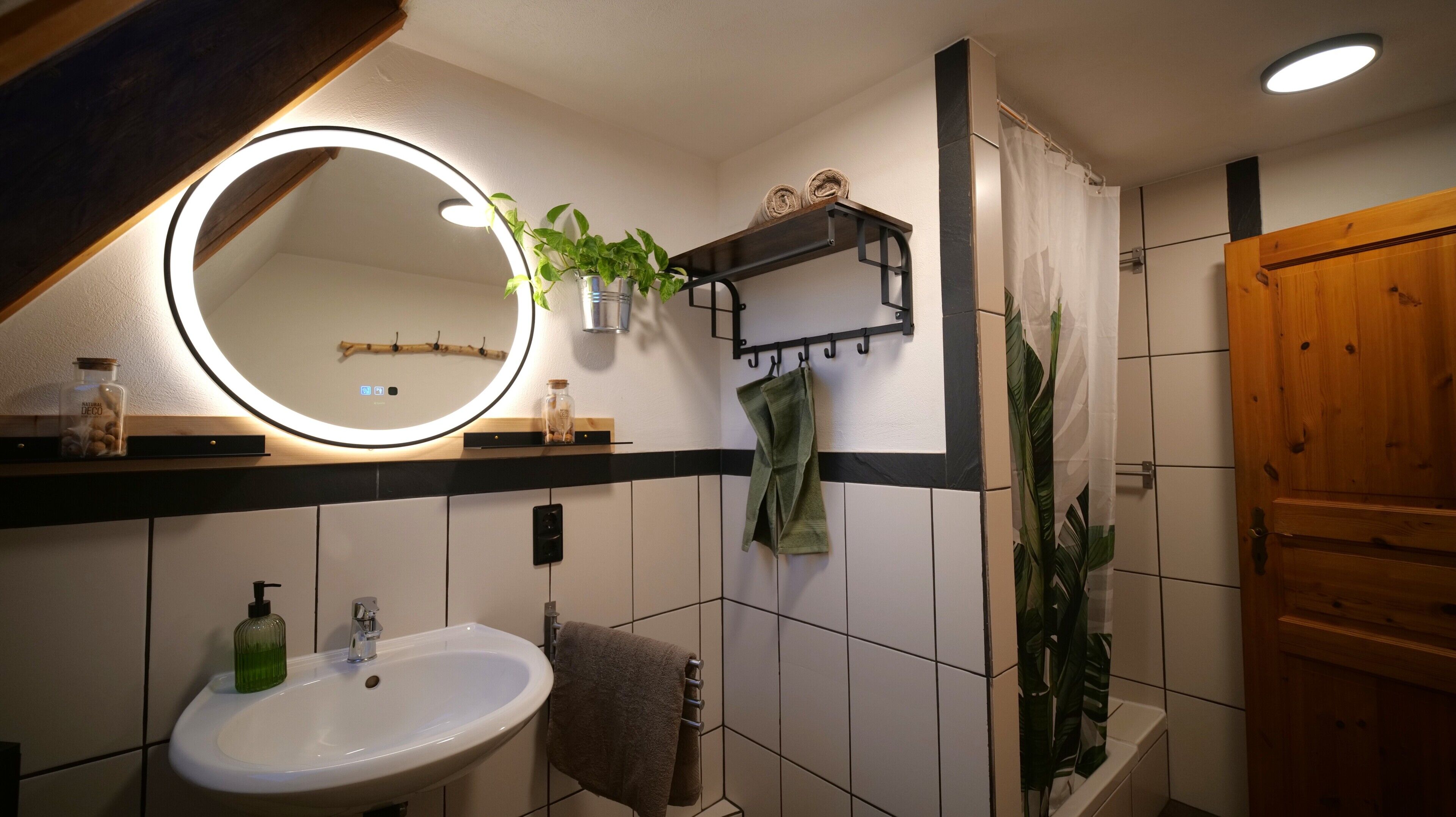 A bathroom with a white sink, a mirror with a light, a towel rack, and a shower curtain.