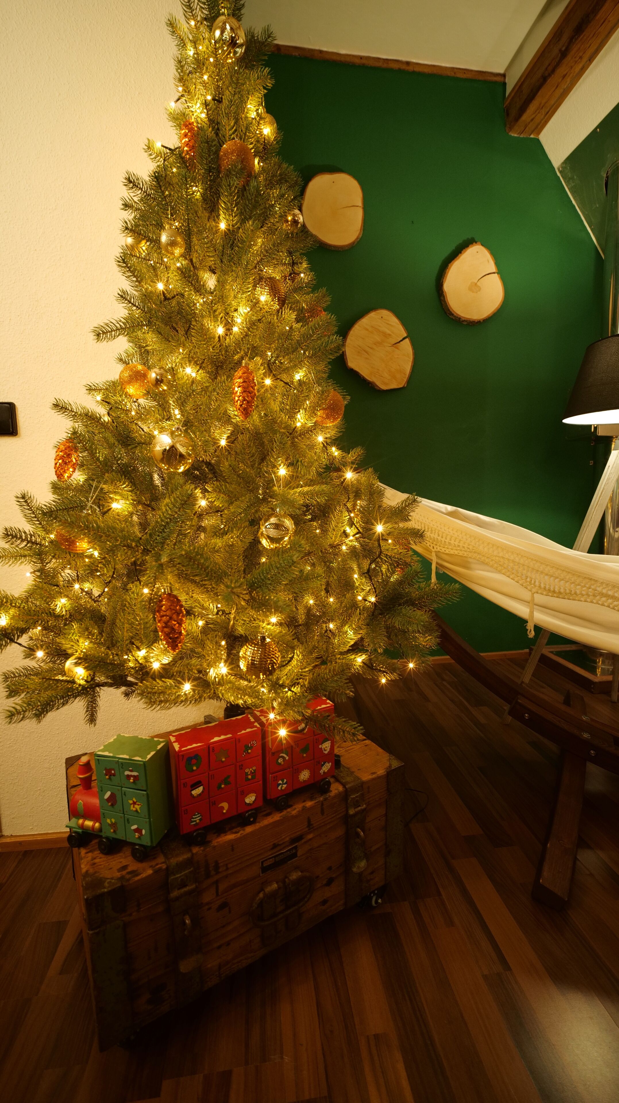 A Christmas tree with lights and ornaments, placed on a wooden chest with wrapped gifts underneath.