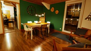 A dining area with a wooden table and chairs, a green wall with a clock, and a view of the kitchen through a glass door. - Green Loft Black Forest / 120 sqm / roof balcony -- music corner (Fluorn-Winzeln)