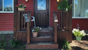 Une maison rouge avec un porche à l’avant, une porte et deux plantes en pot.