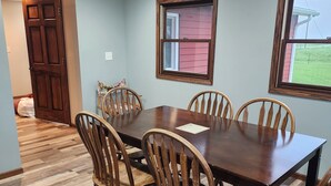 Un coin repas avec une table et des chaises en bois, un ventilateur de plafond et une fenêtre donnant sur l’extérieur.