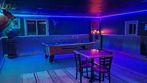 Une pièce faiblement éclairée, avec une table de billard, des chaises et une tête de cerf décorative accrochée au mur.