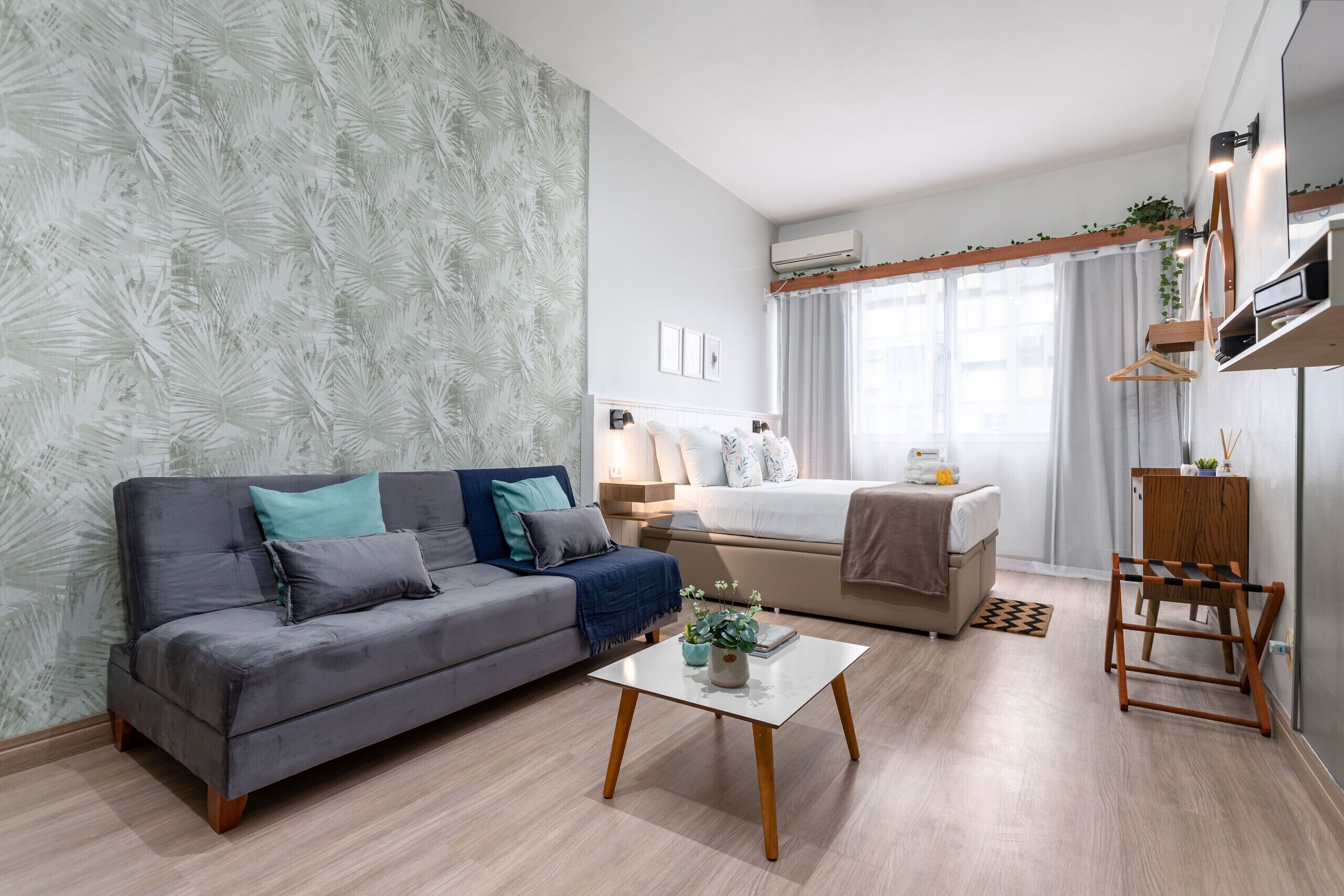A modern living room with a grey sofa, a small coffee table, and a bed with a white headboard.