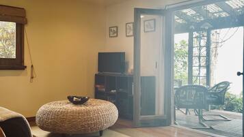 A cozy living room with a television, wicker ottoman, and a wooden chair.