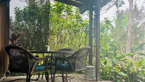 Une terrasse extérieure en bois, dotée de meubles en osier et d’un tapis à motifs.