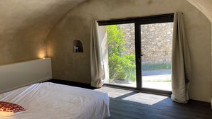 Un dormitorio con cama, una pequeña estantería y vistas a zonas verdes a través de una puerta corredera.