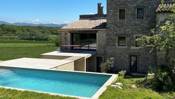 Un edificio de piedra con piscina, patio y vistas al campo.
