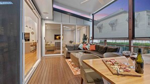 Un espacio exterior moderno con terraza de madera, mobiliario de mimbre y una mesa de comedor lista para una comida.