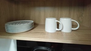 Una repisa de madera con una pila de platos blancos y dos tazas blancas.
