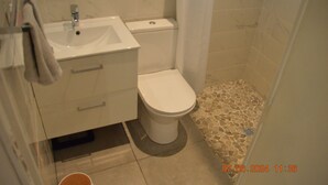 Un baño con lavamanos blanco, inodoro y suelo de baldosas.