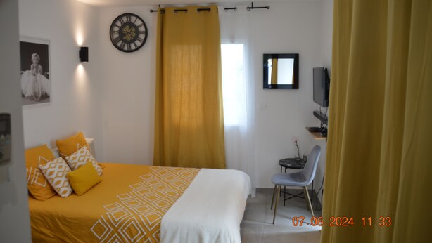 Habitación de hotel con cama, escritorio, silla, reloj y televisor.