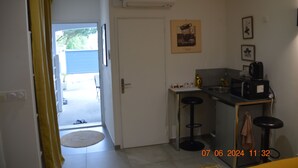 Una cocina compacta con microondas, cafetera y taburetes de bar. Una puerta da a un espacio exterior.