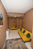 A room with a yellow sofa, a small table, a wall-mounted heater, and a picture of a village.