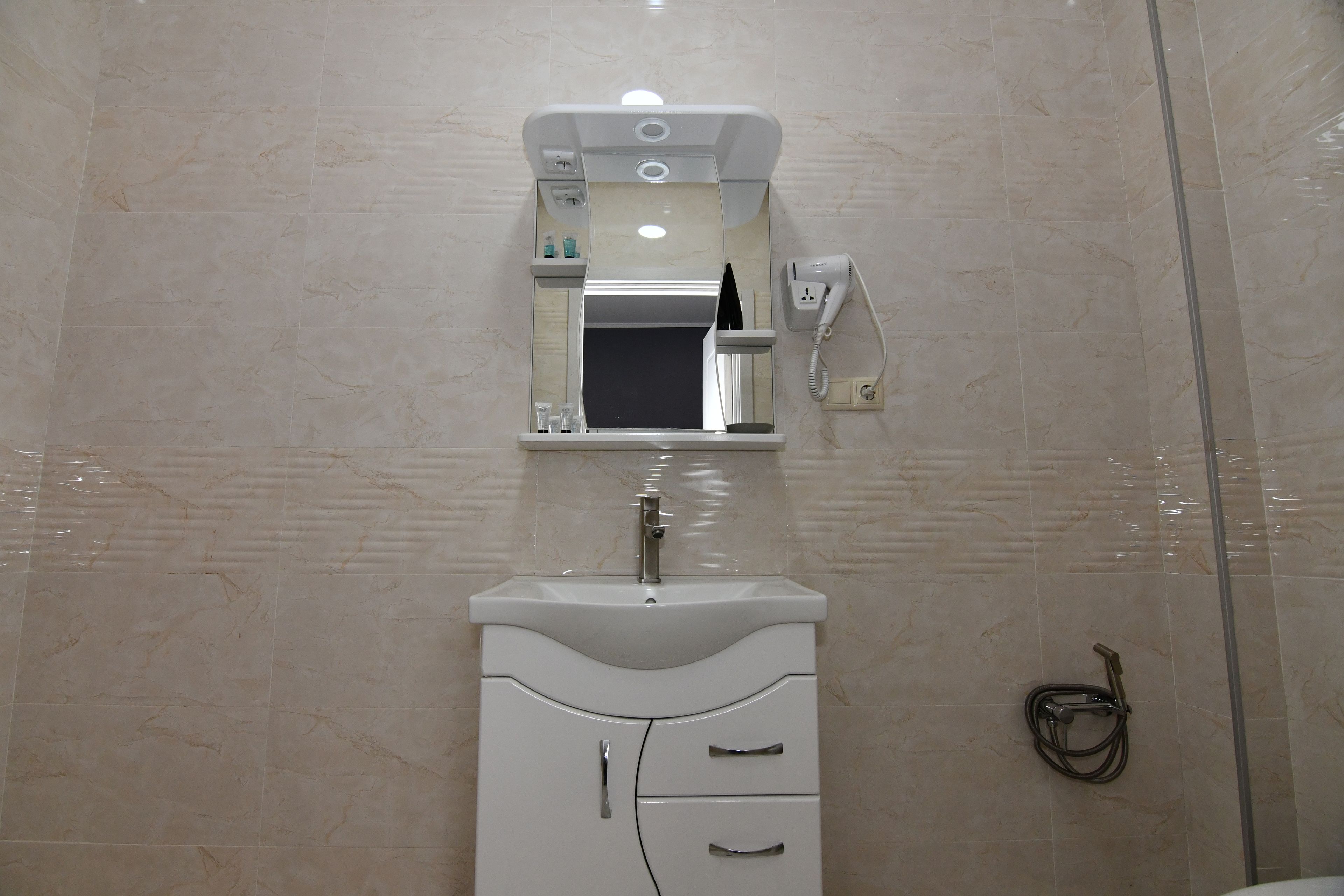 Un baño con lavamanos blanco, espejo y toallero.