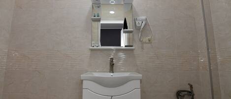 Un baño con lavamanos blanco, espejo y toallero.