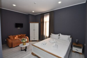 Una habitación de hotel moderna con cama, sofá, televisor, armario y una pequeña mesa con un jarrón de flores.