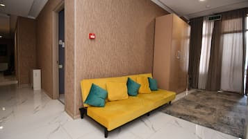 Un hall de hotel con un sofá amarillo, una luz de emergencia roja y un piso de mármol.