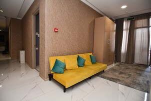 A hotel lobby with a yellow sofa, a red emergency light, and a marble floor.