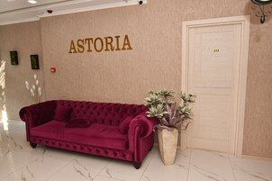 Un sofá rojo y confortable en un vestíbulo con un letrero en la pared que dice 'ASTORIA' y una puerta marcada con el número '222'.