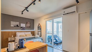 Una habitación de hotel moderna con cama, escritorio con silla, espejo y balcón con vistas a la ciudad.