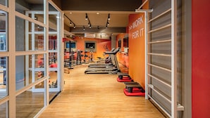 Un gimnasio con cintas de correr, máquinas de pesas y una pared roja con un letrero.