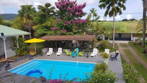 Ein Pool mit Liegestühlen und einer überdachten Sitzgelegenheit, umgeben von üppiger Vegetation und blühenden Pflanzen.