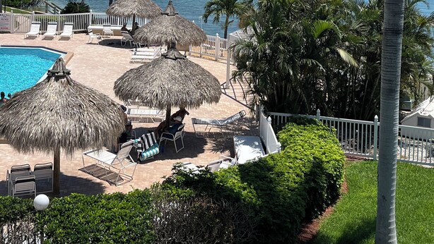A poolside area with lounge chairs, thatched umbrellas, and a view of the sea and buildings in the background.