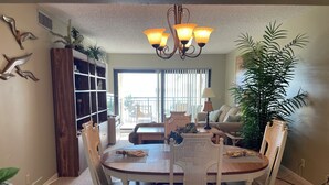 A dining area with a round table, white chairs, a chandelier, and a potted plant.