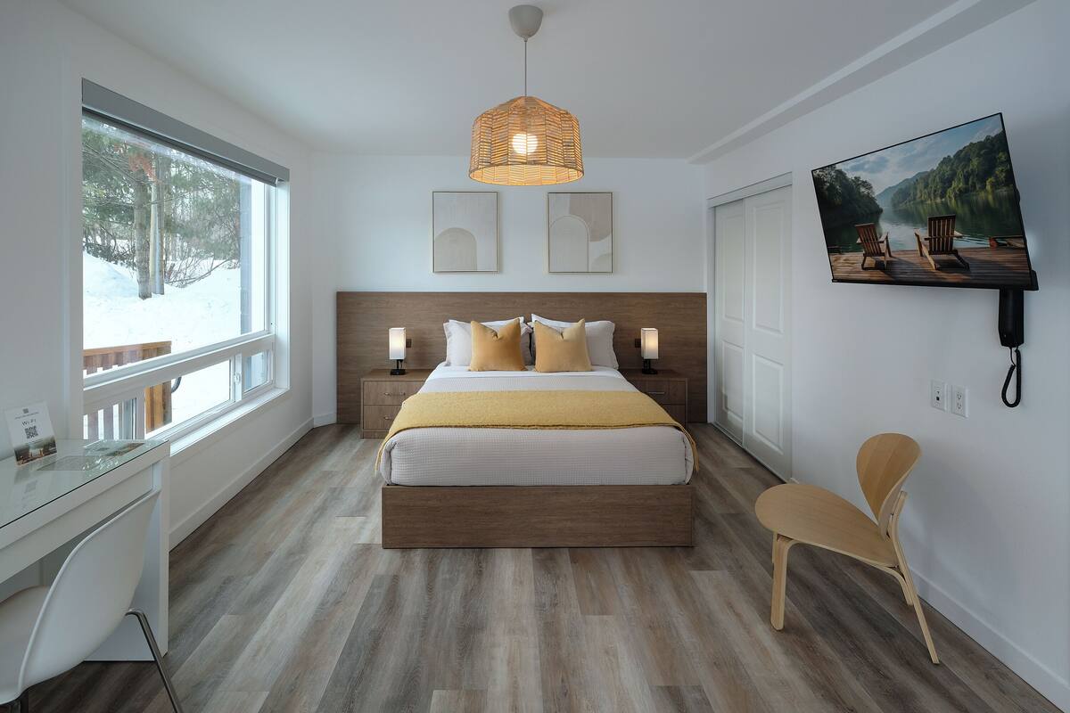 A modern bedroom with a large bed, bedside tables, a desk, and a TV on the wall.