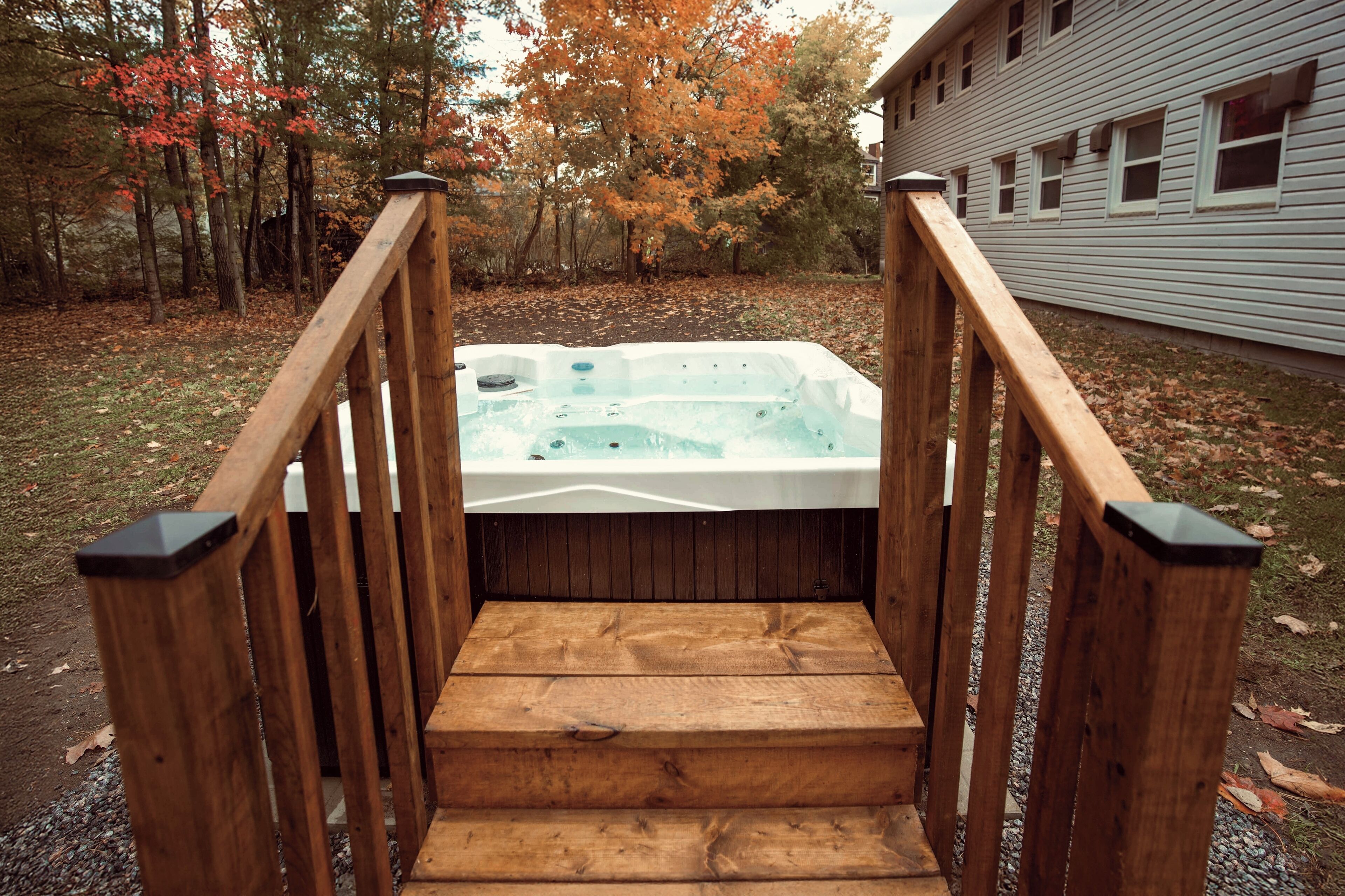 A wooden staircase leading to a hot tub surrounded by trees with autumn foliage.