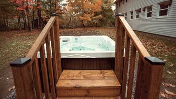 A wooden staircase leading to a hot tub surrounded by trees with autumn foliage.