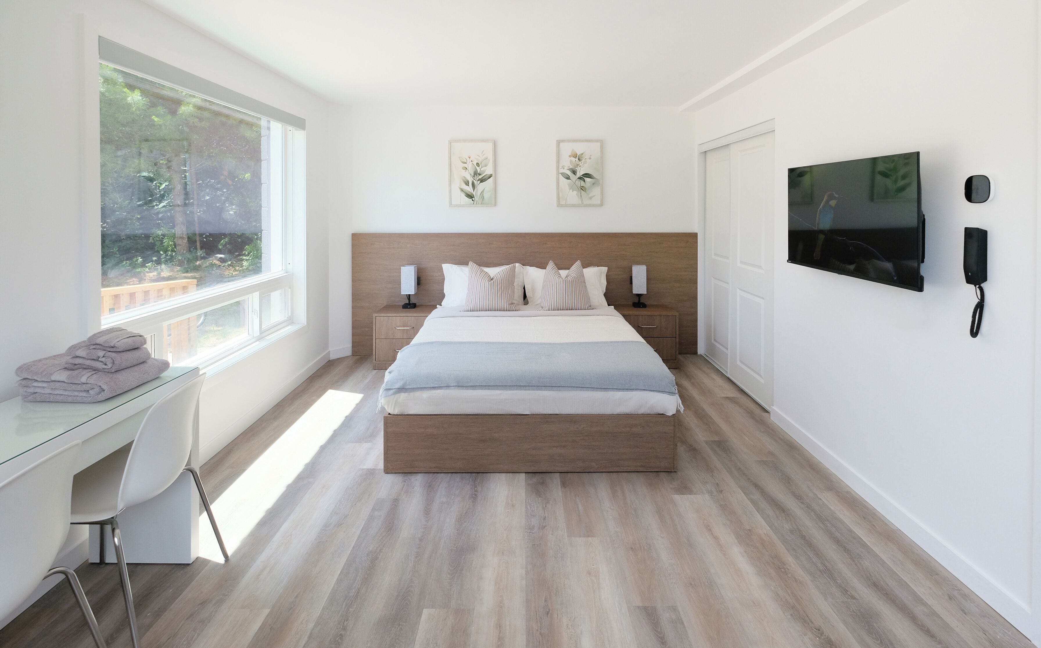 A modern bedroom with a large bed, bedside tables, a desk, and a TV.