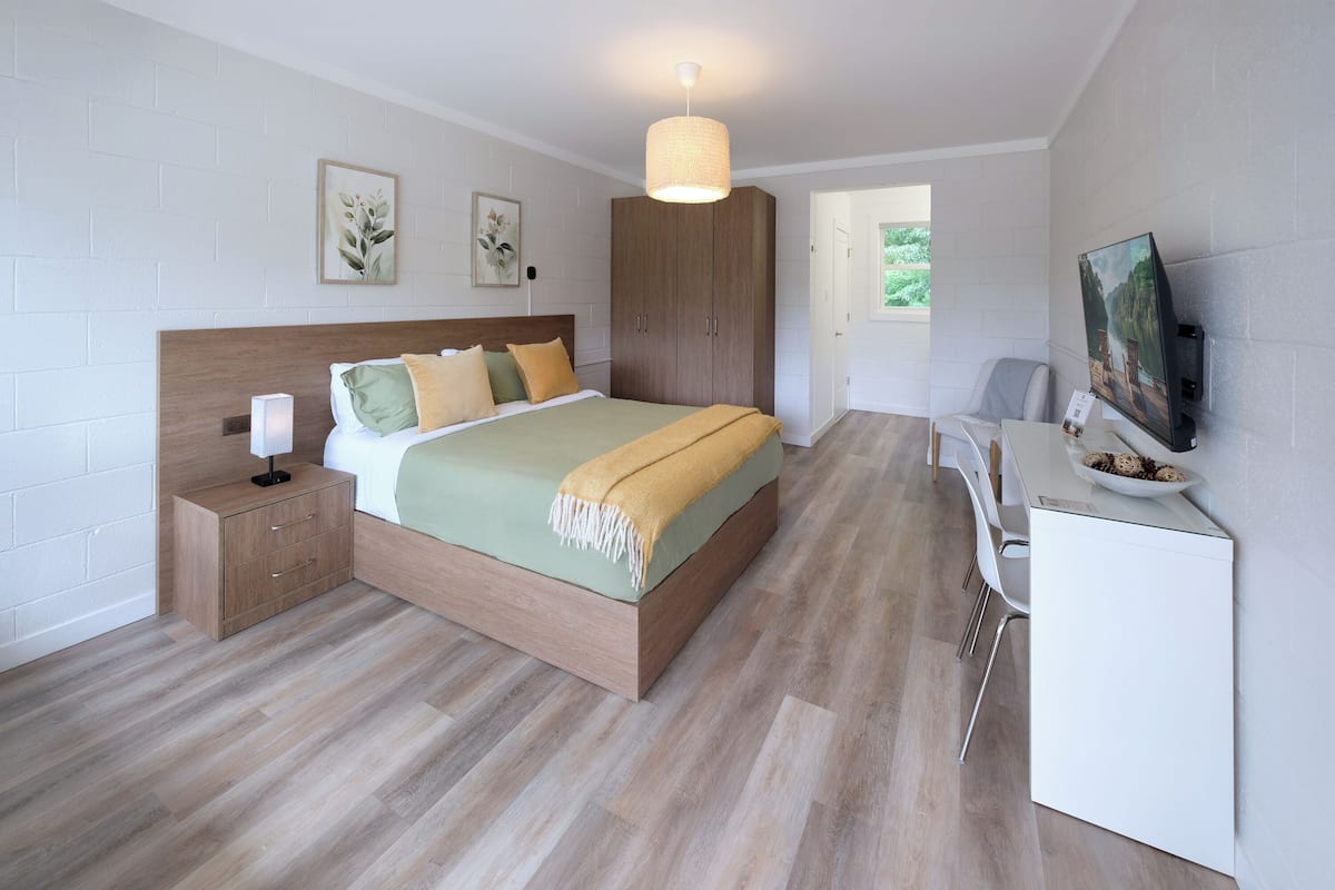 A modern bedroom with a wooden bed, a nightstand, a desk, and a television.