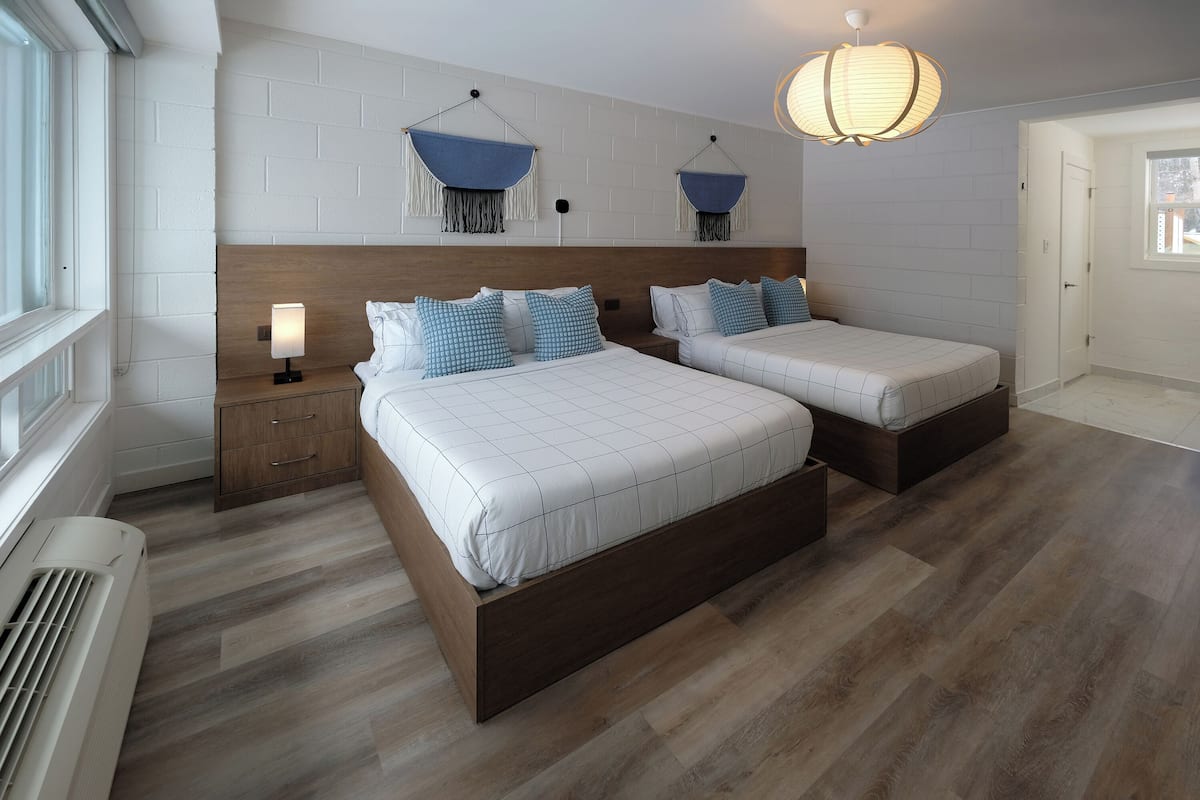 A modern bedroom with two beds, a wooden headboard, a bedside table with a lamp, and a hanging light fixture.