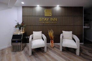 A reception area with two white armchairs, a wall-mounted sign reading "STAY INN MUSKOKA", and a water dispenser. - Stay Inn Muskoka (Gravenhurst)