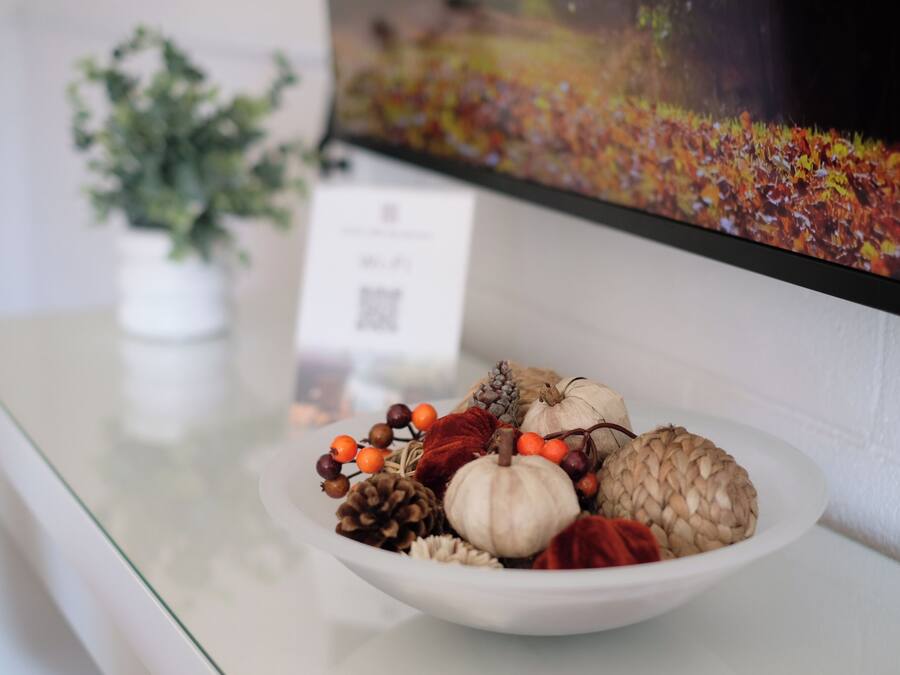 En skål med säsongsbetonade dekorationer står på ett bord tillsammans med en krukväxt, och i bakgrunden syns en skylt.