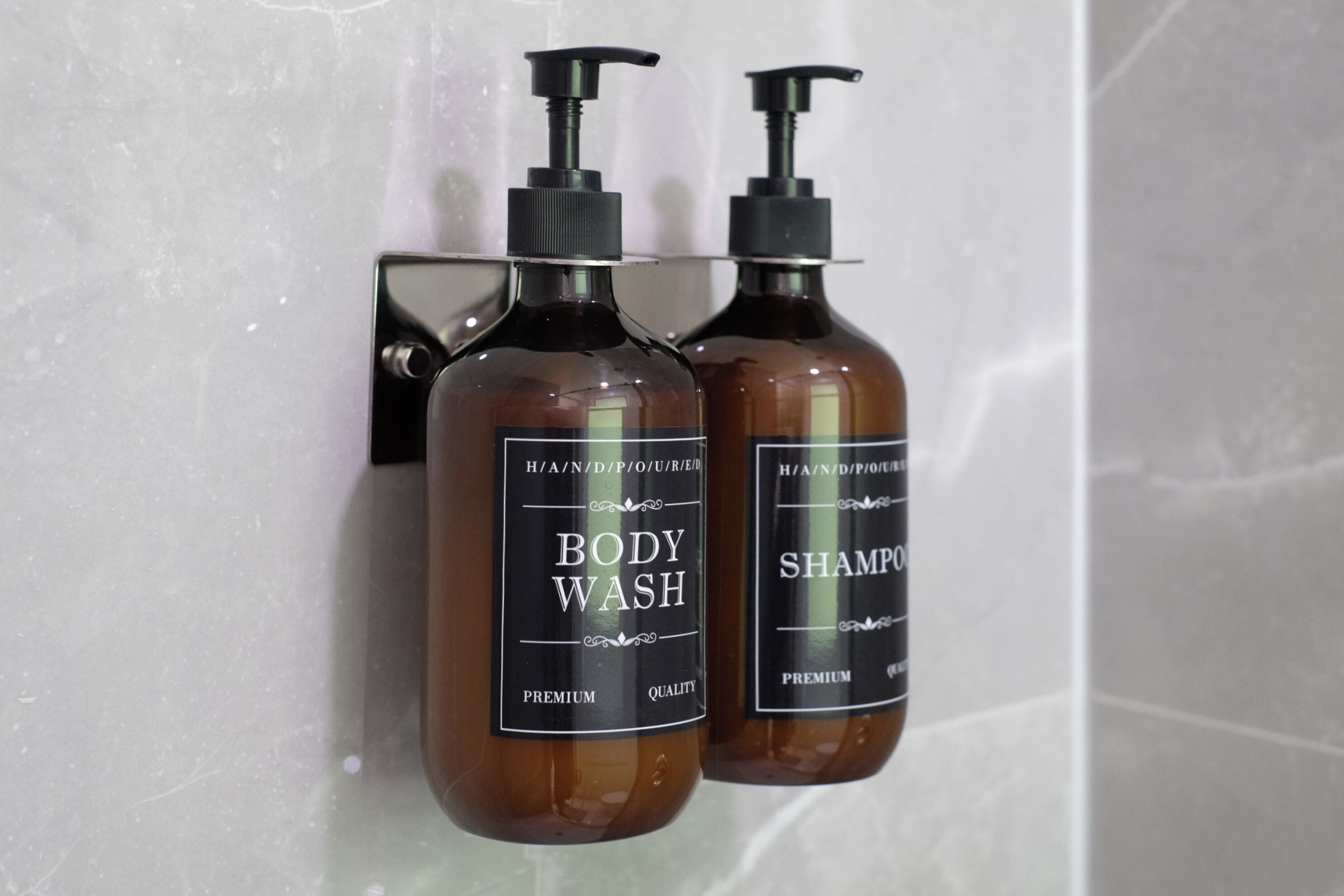 Two brown bottles of body wash and shampoo on a tiled wall.