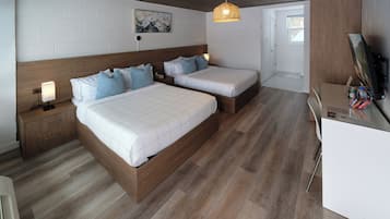 A modern bedroom with two beds, a wooden headboard, a nightstand, a desk with a computer, and a wall-mounted TV.