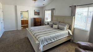 A bedroom with a bed, a ceiling fan, a dresser, a vanity with a mirror, and a window with blinds. - Cozy 4 bedroom family getaway home. Pet friendly home.  (Turlock)